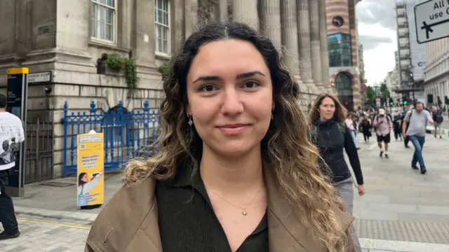 A woman with curly brown hair and brown jacket