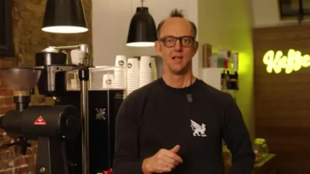 Peter Dore-Smith is pictured speaking in front of a coffee-making machine.