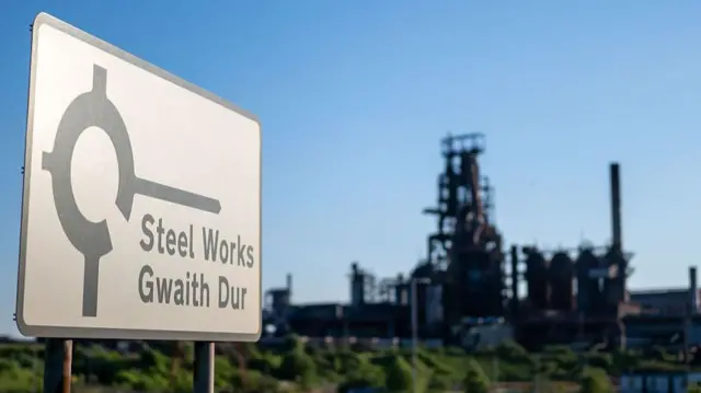 A road sign showing the steel works with the steel works in the background.