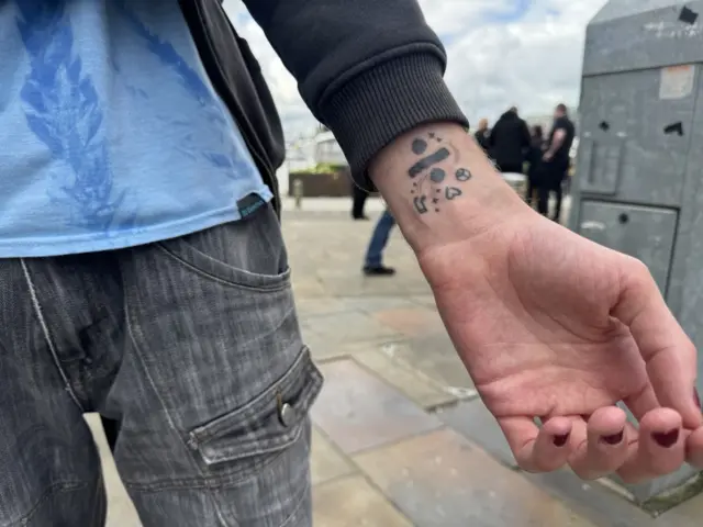 Divide symbol, amongst other tattoo pieces on Iris' wrist