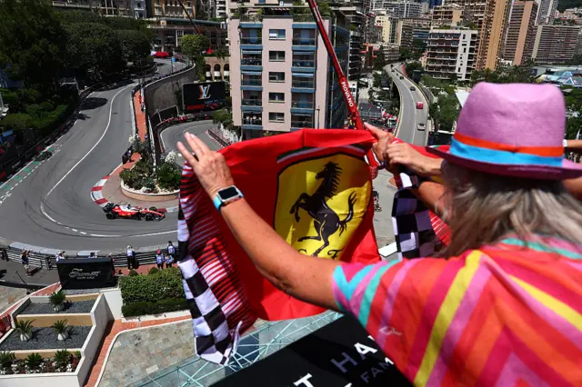 A fan holds up a Ferrari flag as Charles Leclerc drives past the hairpin