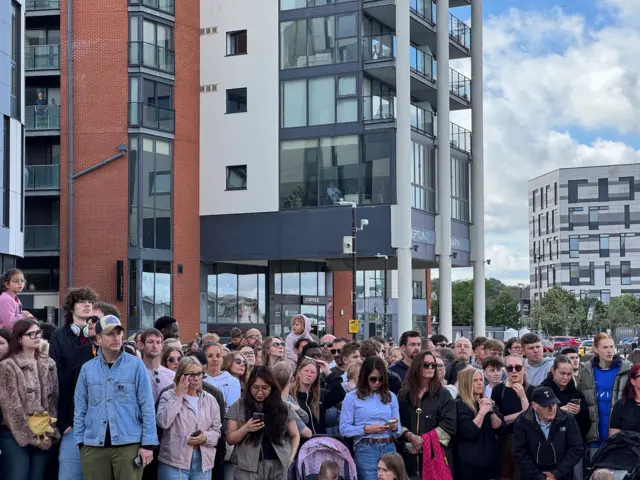 A crowd of people ready to see the singer and there are people sitting in their offices peering over the crowds to the performance