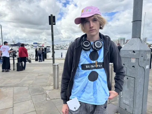 Iris is wearing a hat, headphones, and a blue tie-dye t shirt, with Ed Sheeran's Divide album on