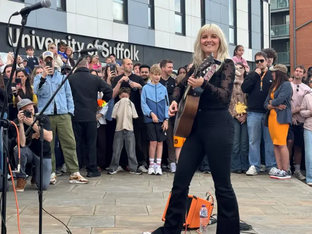 A singer wearing all black holding a guitar and performing to a crowd