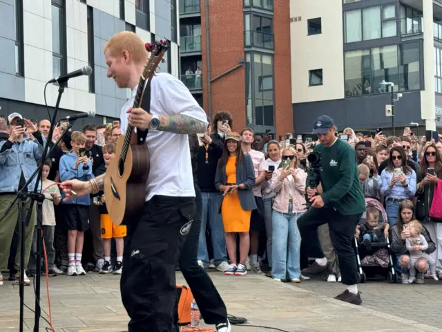 Ed holding a guitar with big crowds behind