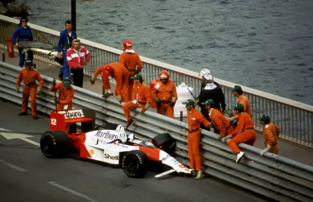 Marshals climb over the barrier to attend to the crashed McLaren of Ayrton Senna at the 1988 Monaco Grand Prix