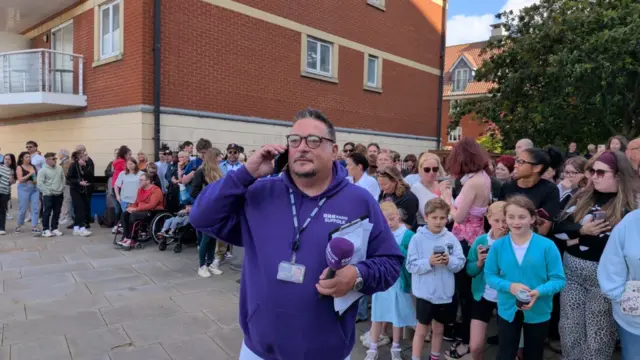 Wayne Bavin, wearing a purple branded BBC hoodie, on the phone