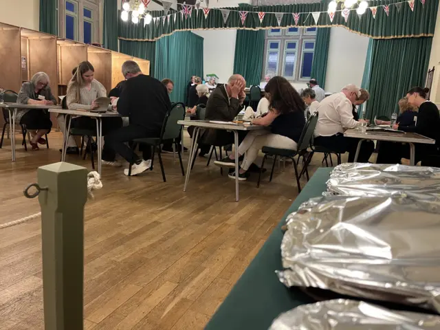 People sitting at tables counting votes on ballot papers