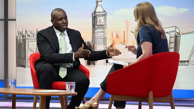 David Lammy (L) in a black suit gesturing with his hands while answering questions. In front of him, sitting in a matching chair, is Laura Kuenssberg