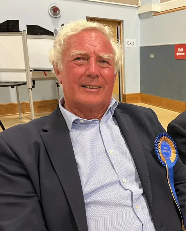 A picture of David Johnson smiling at the camera. He is wearing a blue rosette.