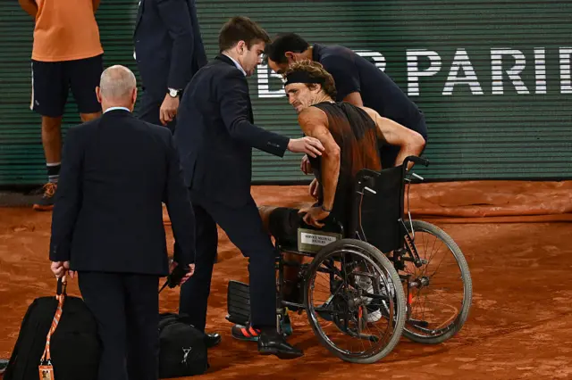 Germany's Alexander Zverev (R) is assisted as he leaves the court in a wheelchair
