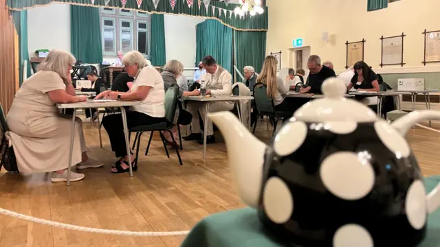 People sitting at tables counting votes on ballot papers