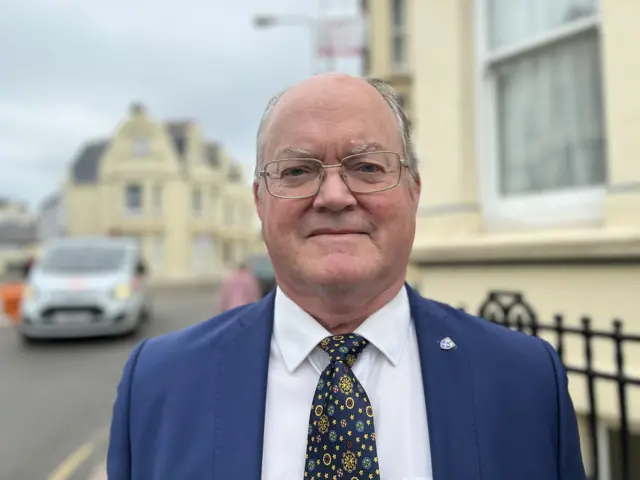 Man in blue jacket, white shirt and blue and yellow patterned tie