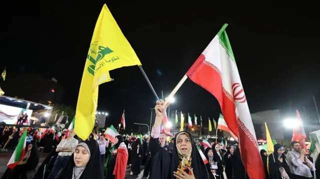 A woman holds the flag of Iran and Hezbollah at a protest.
