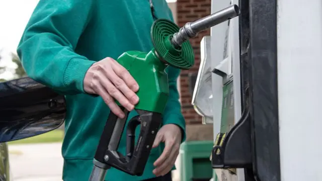 A man in a green jumper returns a green fuel pump at a petrol station