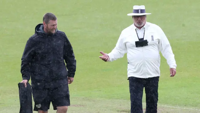 The umpire talks to ground staff as the rain arrives at the Oval