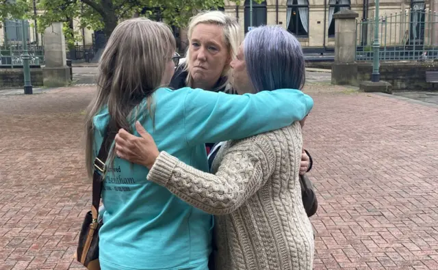 Three women hug outside a court building