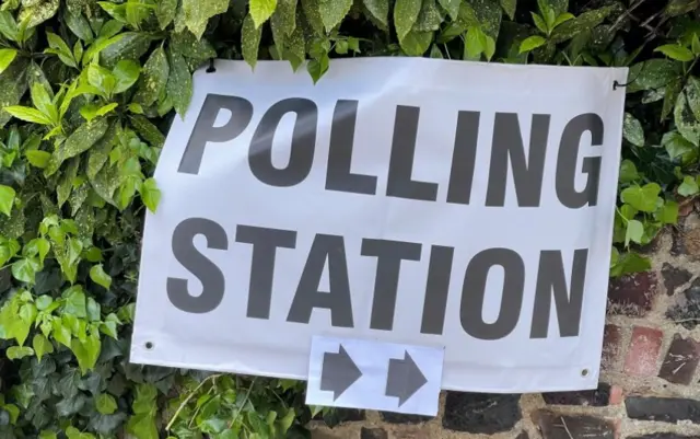 sign saying polling station on a wall with green ivy on it