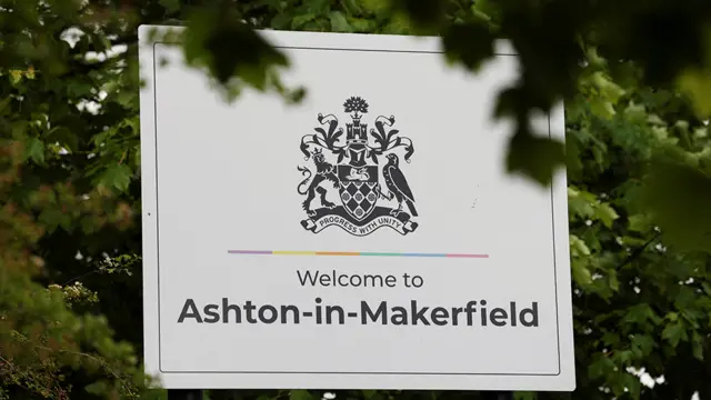 White sign which reads: 'Welcome to Ashton-in-Makerfield' surrounded by trees