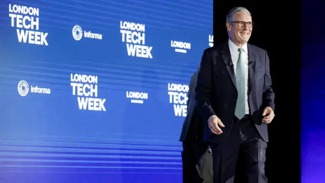 Keir Starmer walking on stage, in front of a back drop advertising London Tech Week