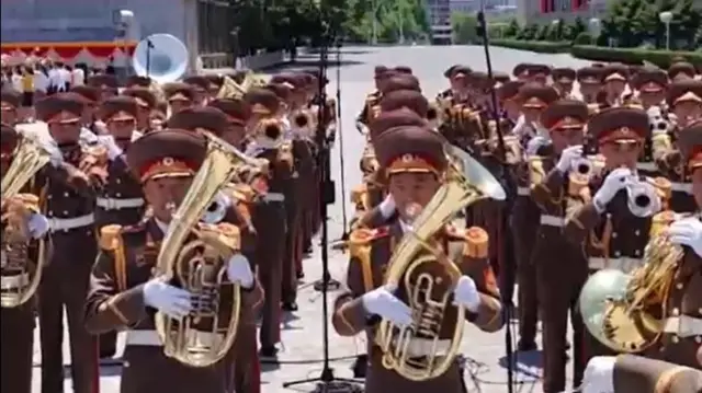 Lines of people in North Korean ceremonial uniforms blow into brass instruments