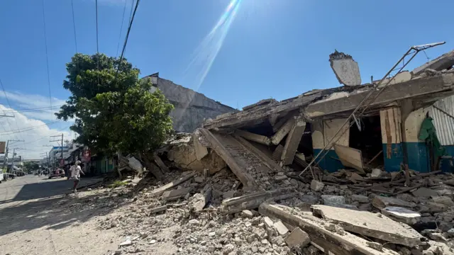 Wide shot of a man walking by the massive rubble of a building that collapsed during an earthquake in the southern Philippines