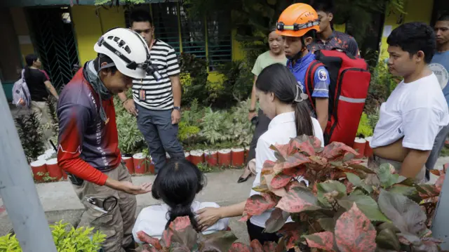 Emergency workers talk to a student, who is seated and with her back to the camera, following an earthquake in Davao City in the Philippines