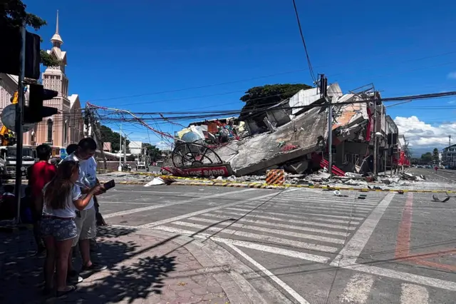 People look at a collapsed building after an earthquake on General Santos City in the Philippines