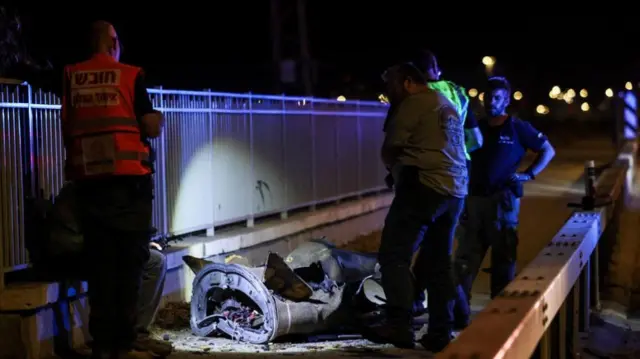 Israeli security and rescue personnel next to a part of a projectile following a missile attack from Iran