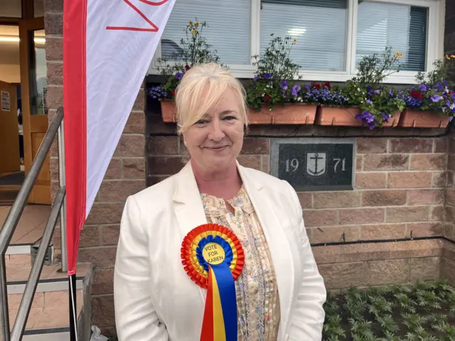 Woman smiling wearing a large rosette in front a brick building