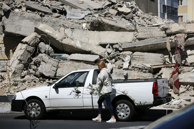 Woman walking past a car parked next to a mound of rubble