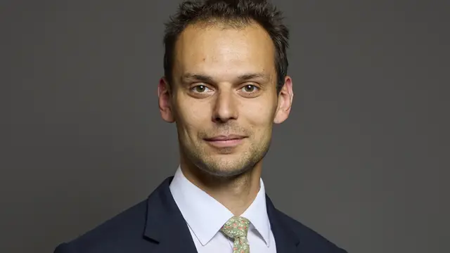 Josh Simons with dark brown hair and brown eyes wearing a suit and tie
