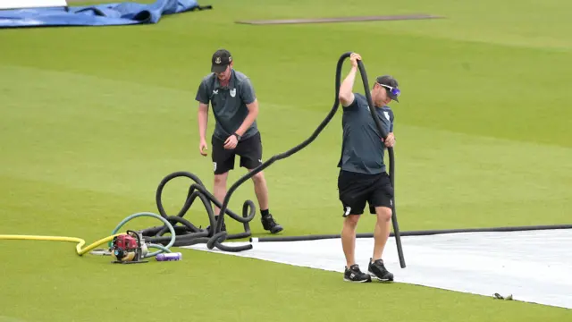 Ground staff remove water from the covers at the Oval
