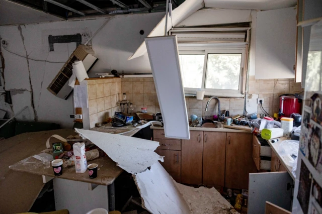 A light is hanging from the ceiling above parts of broken plasterboard which have fallen from above onto a countertop inside someone's kitchen