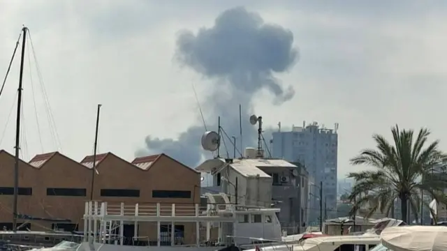 A large smoke cloud rising, boats can ve seen in the foreground