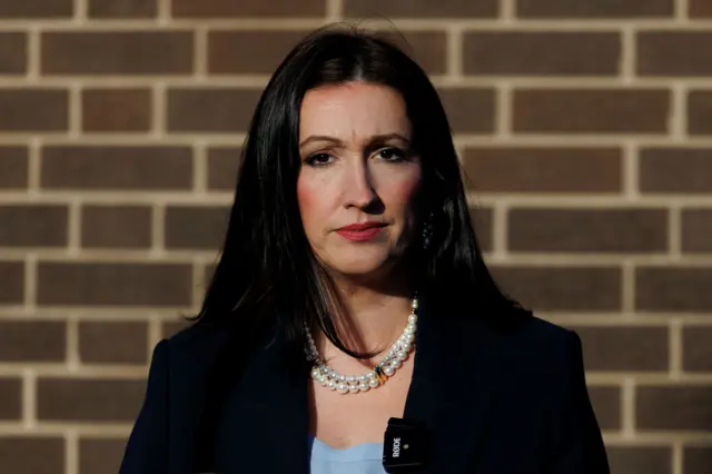 Emma Little-Pengelly, mid-shot, dark hair, wearing a black blazer and blue top