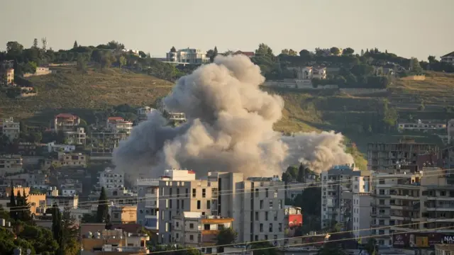 A plume of grey smoke rises from an area with what appear to be residential buildings