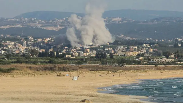 A photograph taken from the southern city of Tyre shows people sunbathing on the beach as smoke rises from the site of an Israeli airstrike in the village of Deir Qanoun Ras al-Ain on June 8, 2026