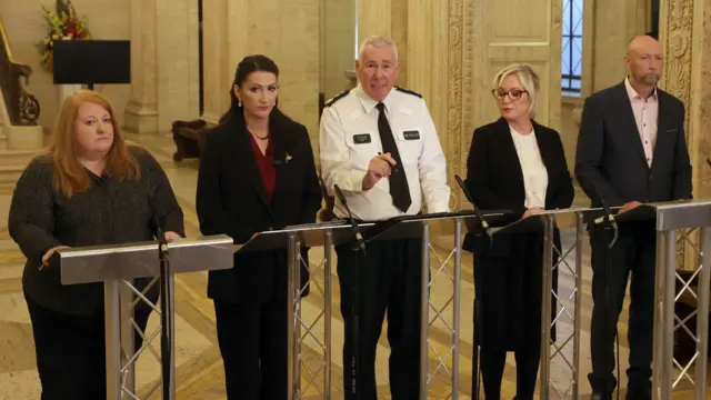 A press conference with five people standing behind podiums