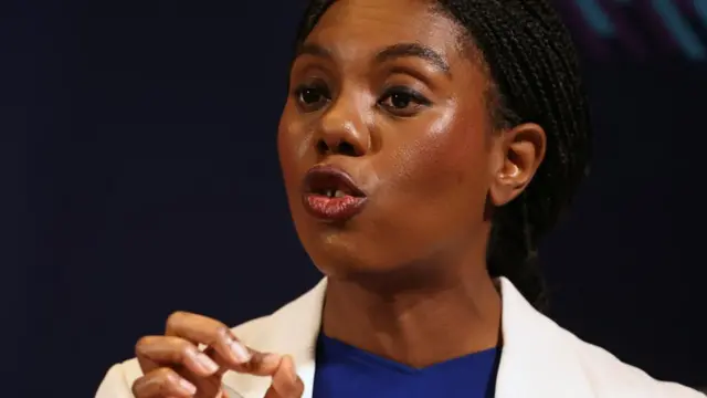 Conservative Party leader Kemi Badenoch speaking and wearing a white blazer and blue top.