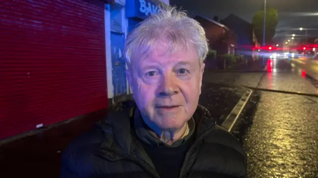 A man with white hair looks at the camera