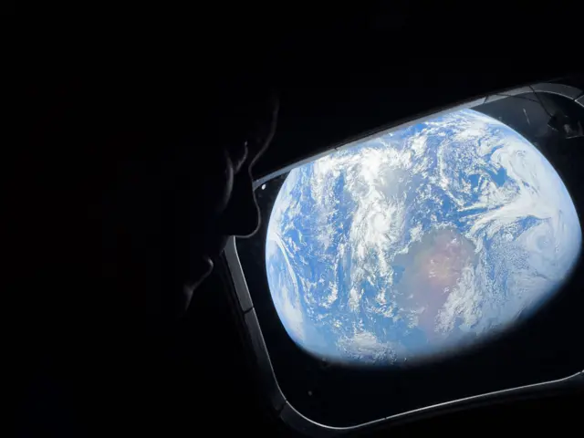 NASA astronaut and Artemis II Commander Reid Wiseman peers out of one of the Orion spacecraft's main cabin windows, looking back at Earth