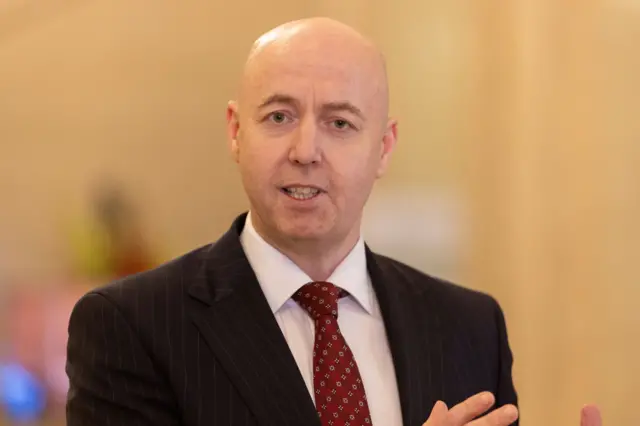 Jon Burrows, midshot, black suit red tie