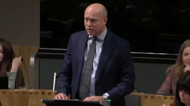 A bald man stands up in the Senedd to speak