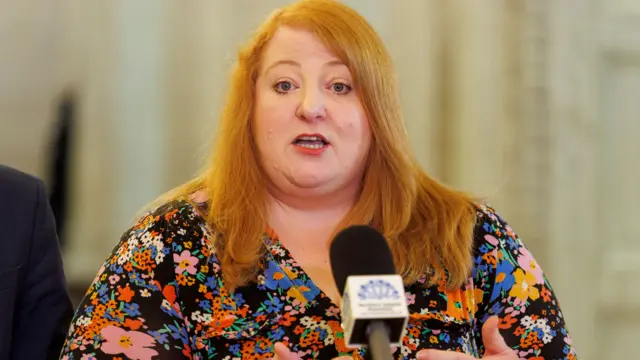 A woman with red hair talking in front of a microphone