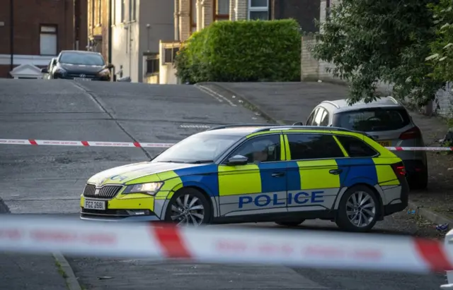 A police car in front of a tape as a road is cordoned off
