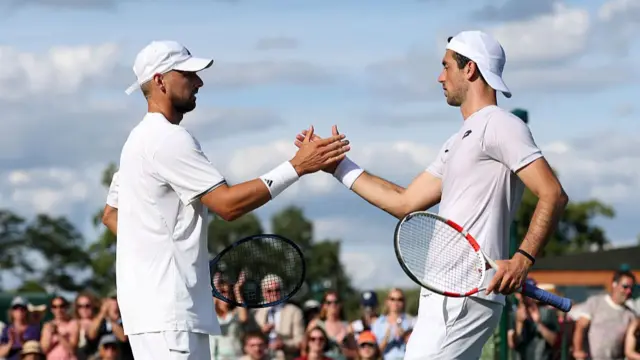 Julian Cash (left), wearing all white and a white cap worn forwards, and Lloyd Glasspool, wearing all white and a cap worn backhands, shake hands