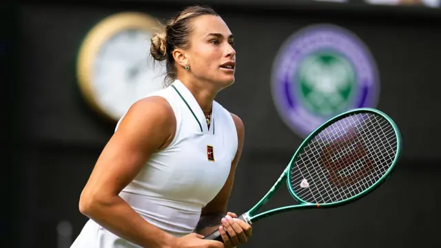 Aryna Sabalenka, wearing a white dress, holding her green racquet in two hands