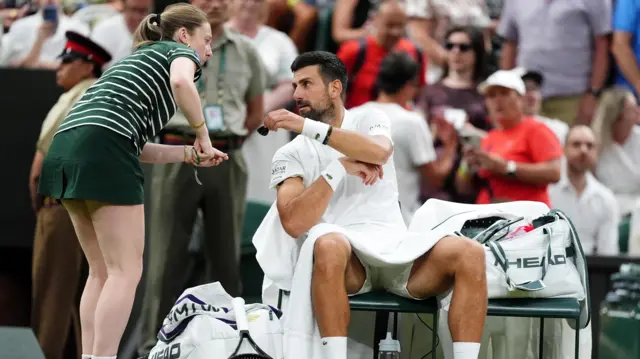 A ball girl cuts off a plaster on the arm of Novak Djokovic