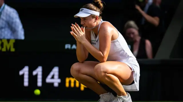 Noskova, wearing all whites, crouches down with her hands together in front of her